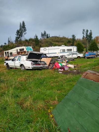 Car with trunk open next to various random items, and two RVs and car in the background.